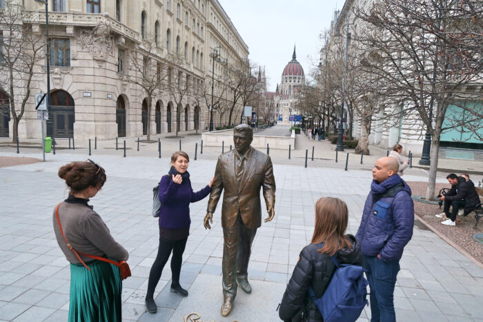 A tour guide standing next to a statue with a small group of people listening intently in Budapest, Hungary