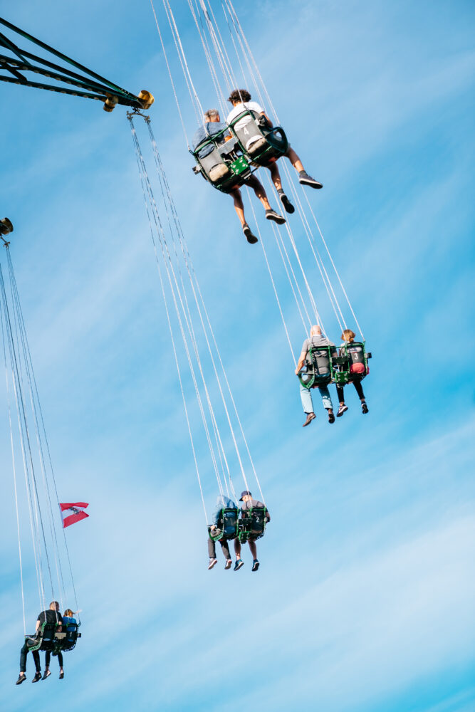 People riding the Prater Tower swing in Vienna, with a bright blue sky and wispy clouds in the background.