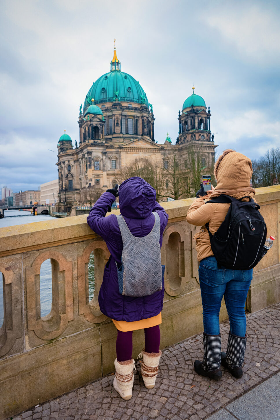 Two kids with backpacks taking photos at the bridge at Berlin Cathedral near Spree River quay in German City centre in Berlin in Germany on a sunny day