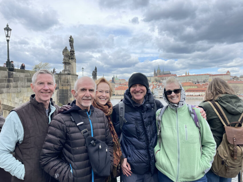 A group of people standing in front of Prague's Charles Bridge, smiling, with Prague Castle in the background