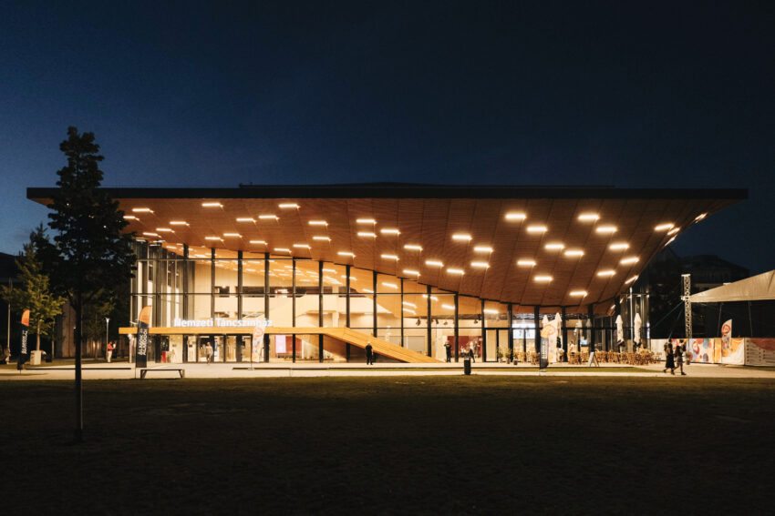 The National Dance Theatre in Budapest, Hungary, at night, with lights glowing out the large glass windows