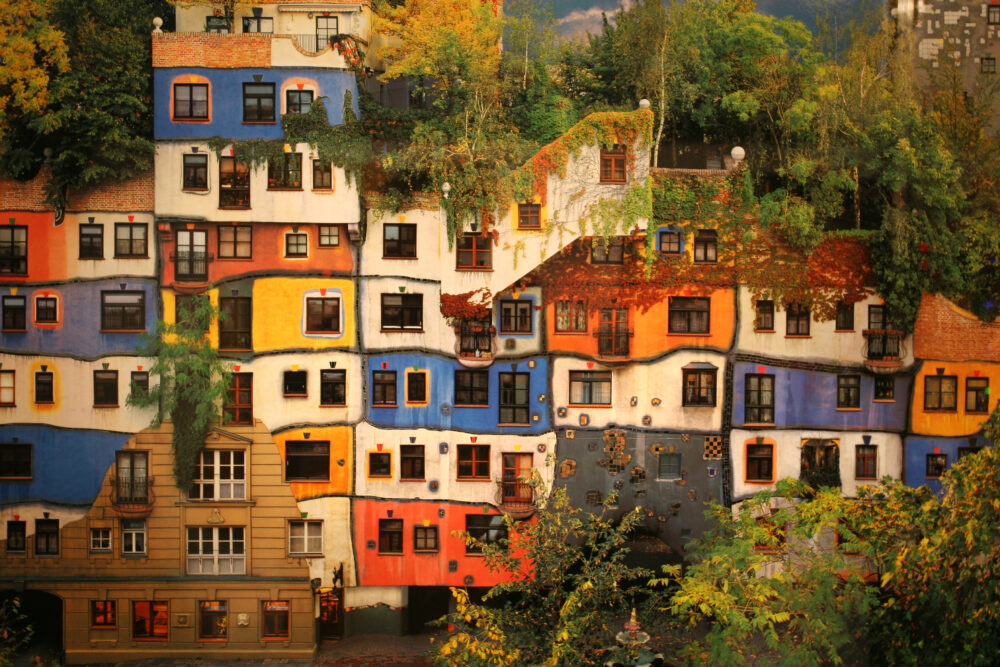 The famous Hundertwasser House in Vienna, with a colorful facade and trees with yellow and gold foliage framing it it