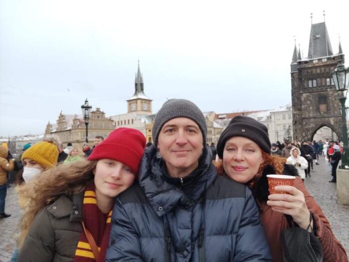 Three people in coats smiling on the Charles Bridge in Prague, Czech Republic