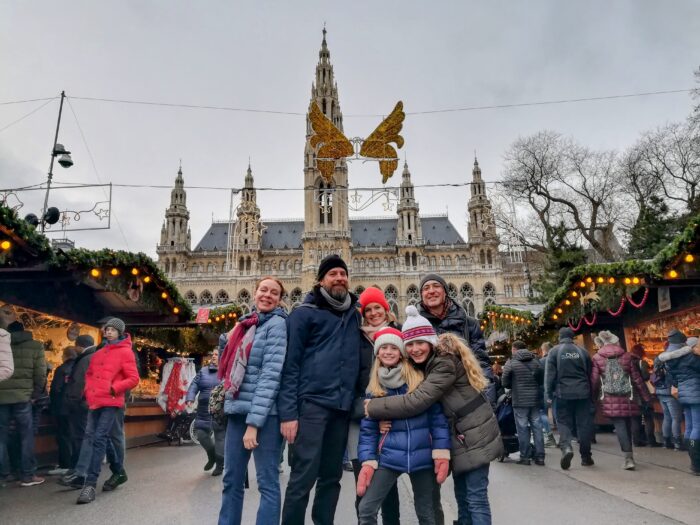 A group of adults and kids posing in front of Vienna's Rathaus at the Christmas market in Vienna, Austria