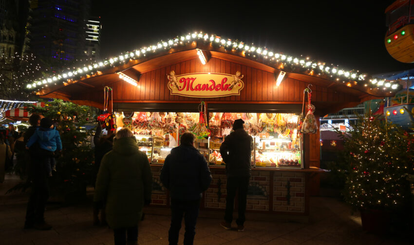 Storefront selling roasted nuts in Potsdam Christmas Market, Berlin, Germany, with people looking at the goods and a Christmas tree next to it