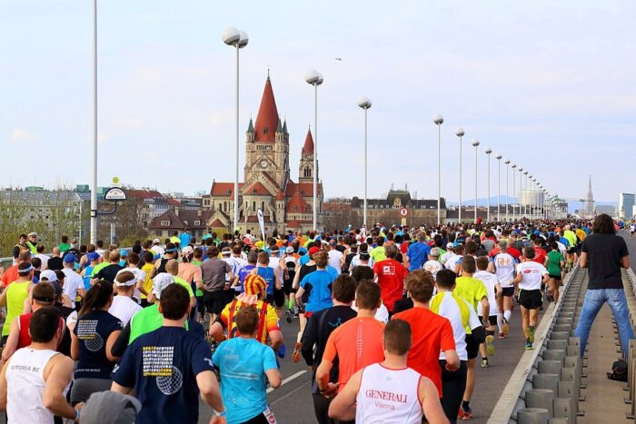 A group of people running across a bridge during the Vienna Marathon with a church in the background