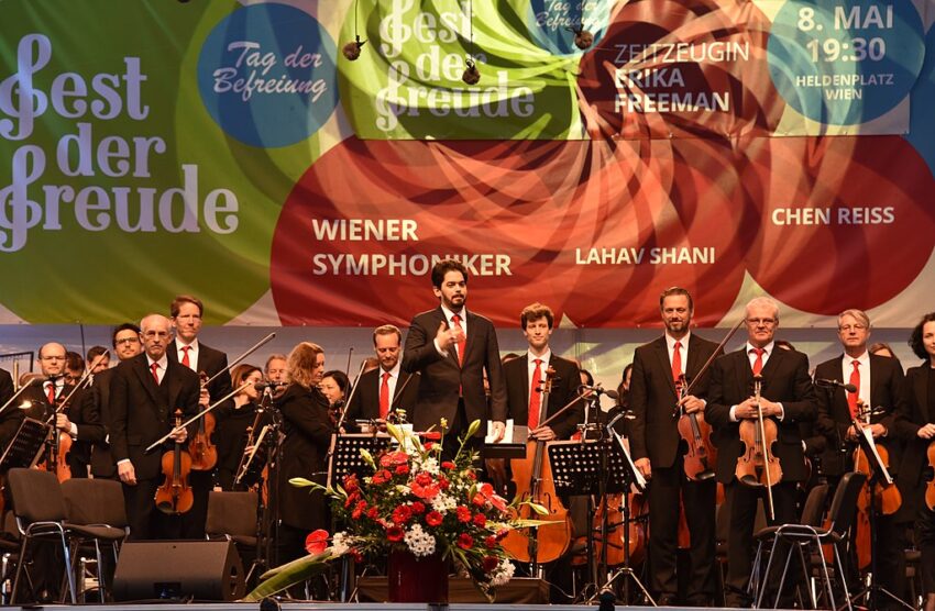 A group of musicians standing on stage, with a colorful banner celebrating Feste der Freude in Vienna