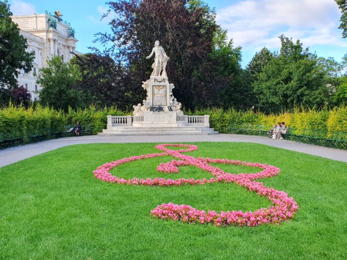 A statue in a park with flowers arranged in a treble clef