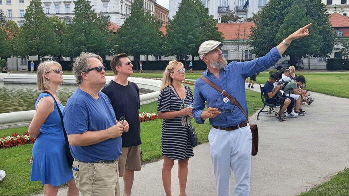 A man in a blue shirt standing outside pointing at something off-camera, with a group of people looking on