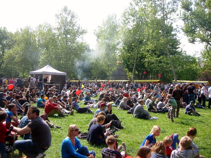 People sitting on the grass on a sunny day in Kreuzberg, Berlin, with some market stalls in the background