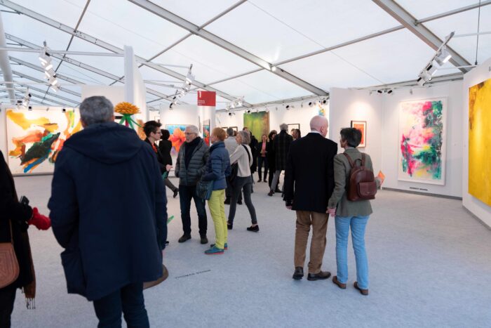 A crowd of people in a white gallery looking at paintings at Art Austria