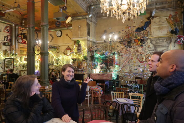 A small group of people standing inside a bar and looking around. the bar has a lot of handmade decorations on the yellow wals