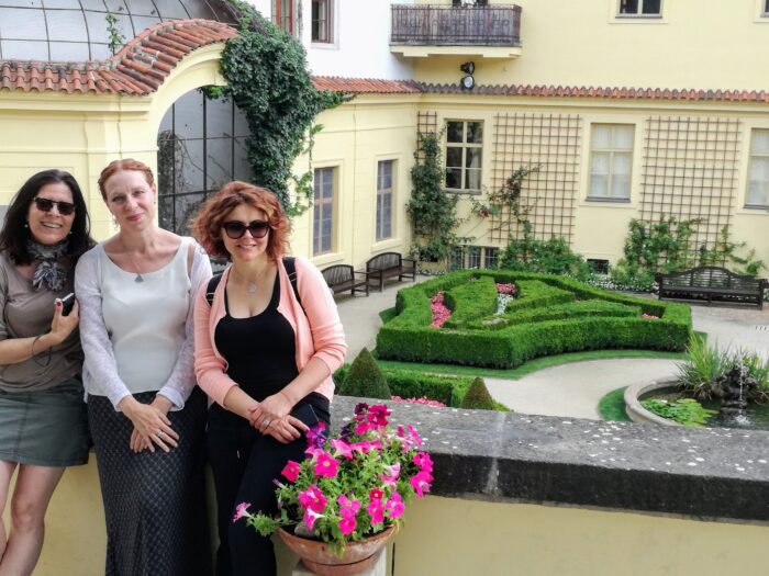 Three women smiling while standing in front of some gardens in Prague