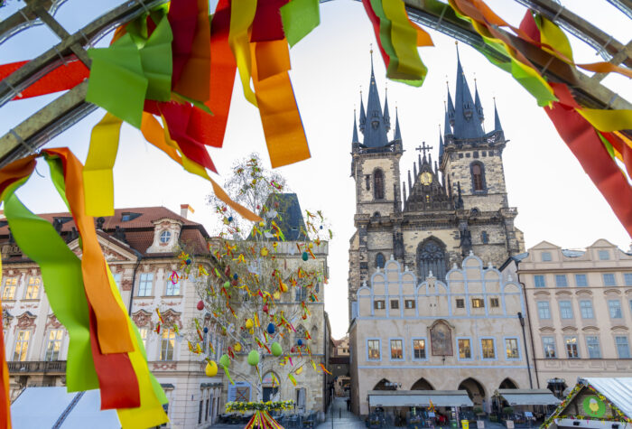 View of Tyn church at old Town Square in Prague, Czech republic, with a tree decorated for Easter in the middle and an arch with ribbons blowing in the wind in the foreground.