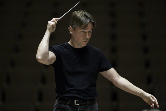 A man in a black t-shirt waving a conductor's baton