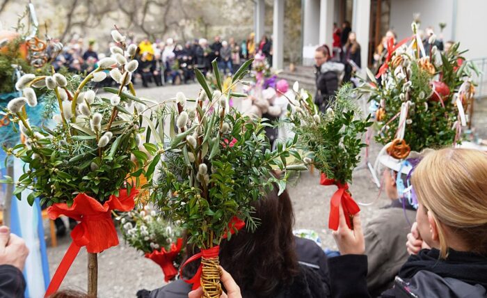 Four traditional Austrian Easter palms - bundles of spring branches tied with a ribbon - held by participants at a Palm Sunday event