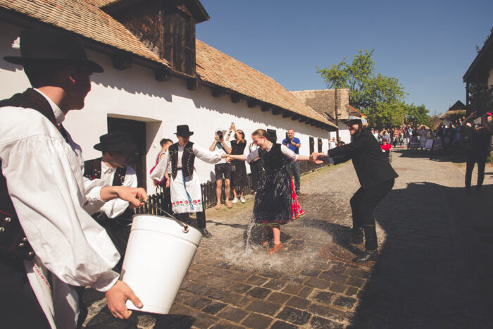 Men and women in traditional clothing in the Hungarian village of Holloko, with one man holding a bucket of water and a woman soaking wet