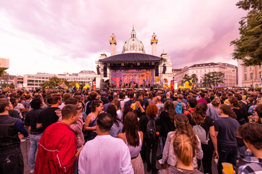 A crowd of festivalgoers looking on at the Popfet Wien mainstage in Vienna, Austria, on an overcast summer day