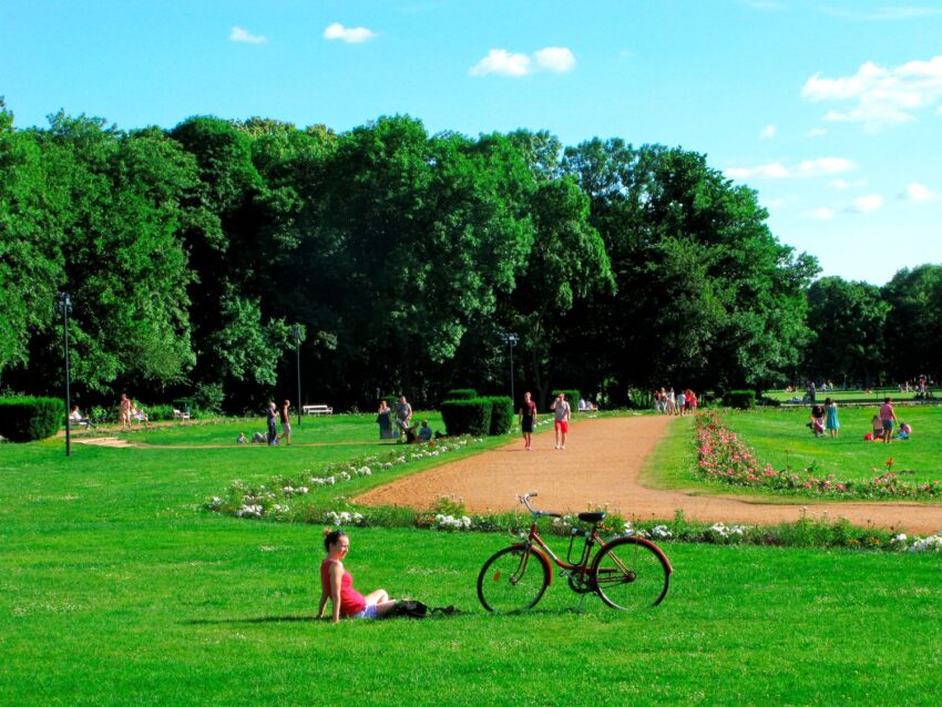 Ayoung woman sitting on the green grass with a bike on a sunny summer day in Margaret Island, Budapest