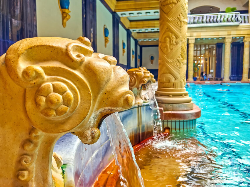 Golden lions spouting water into a pool at Gallert Baths in Budapest, with matching golden columns behind them